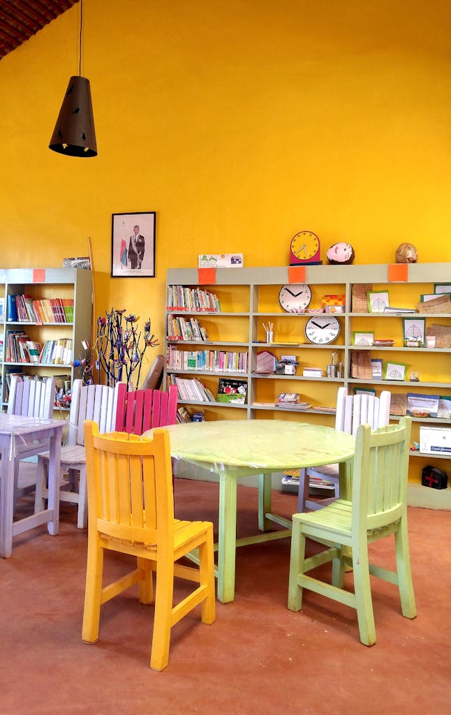 Photo by Nantenaina Andrianjaka A vibrant classroom library featuring wooden shelves and colorful chairs against a bright yellow wall.