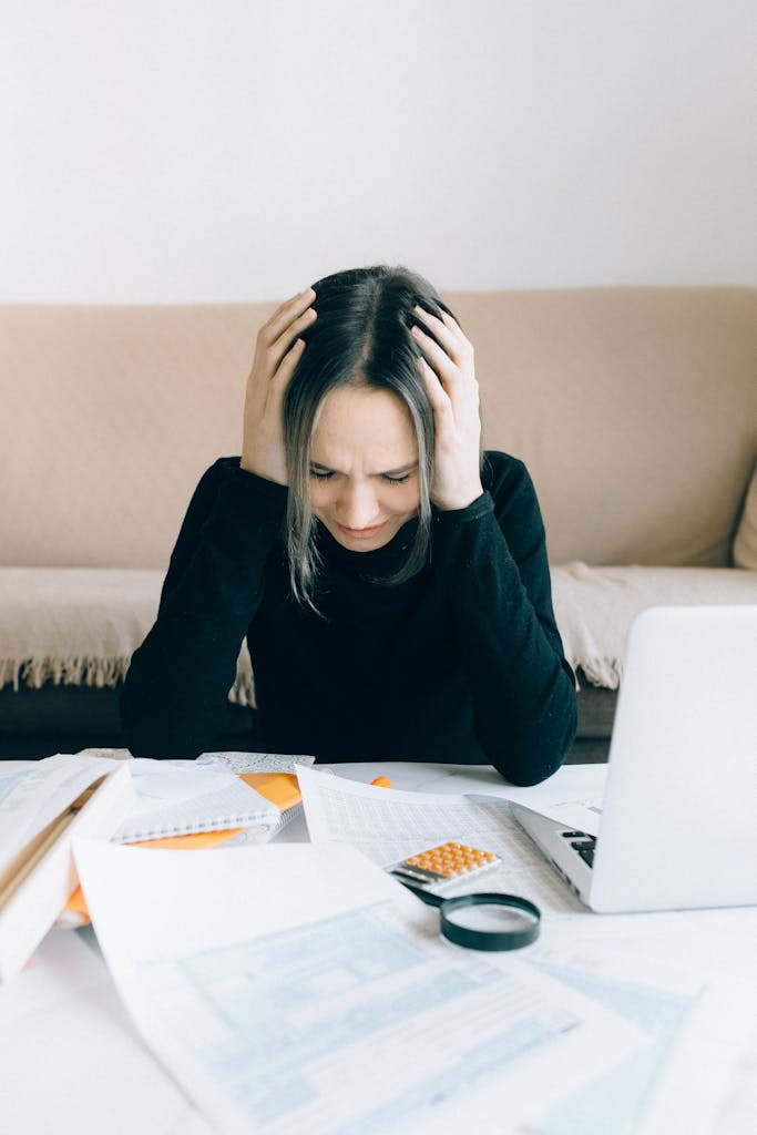 Photo by Nataliya Vaitkevich A woman appears stressed and overwhelmed with paperwork at her home desk.