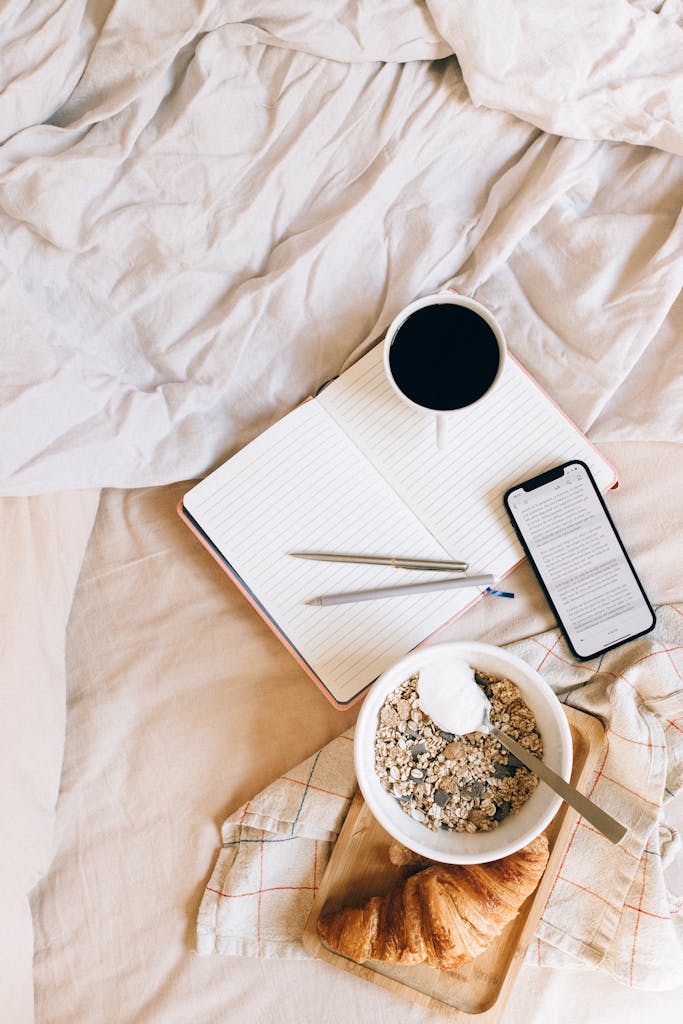 Photo by Nataliya Vaitkevich Flat lay of breakfast with coffee, granola, and croissant on a bed.
